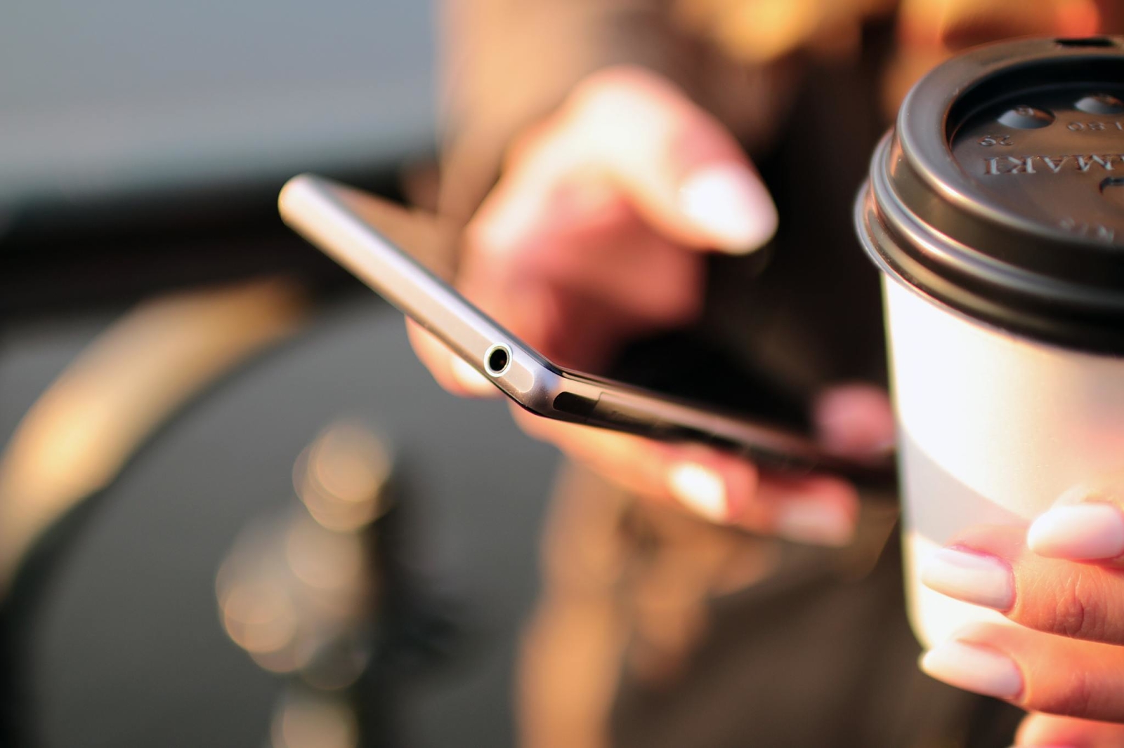 person checking his cell phone, with a coffee in his left hand, selective focus